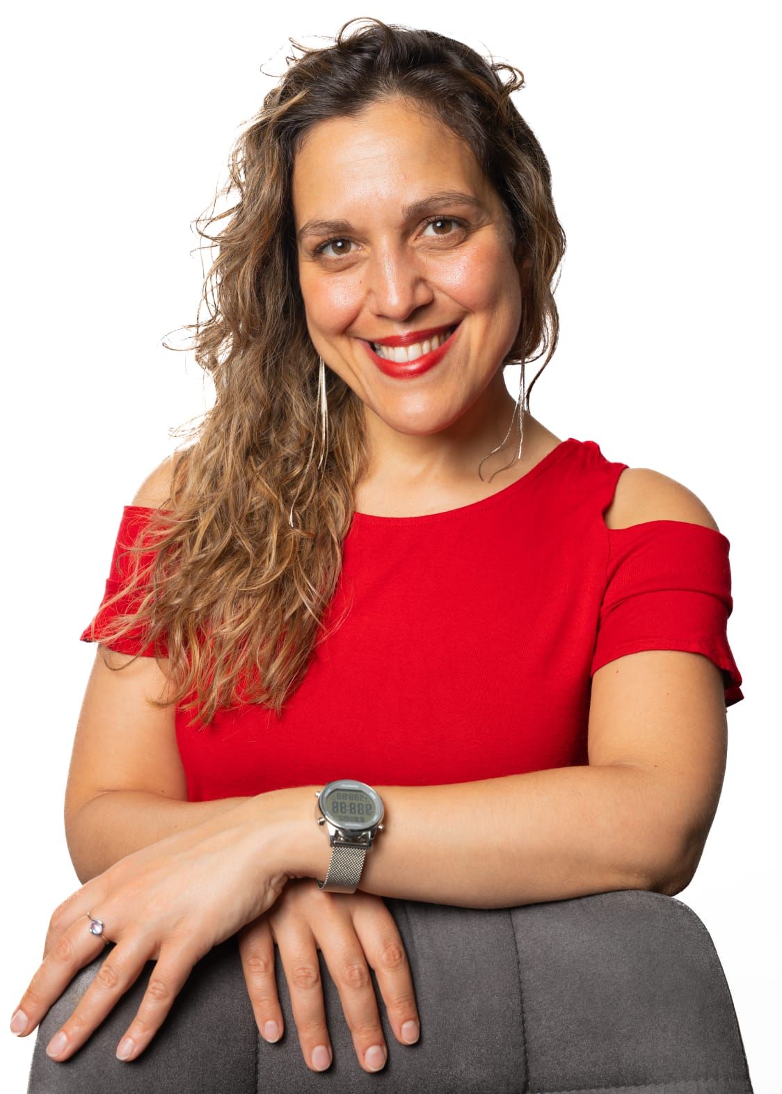 Roberta Nozzolillo in einem roten Oberteil, die Arme auf einer grauen Stuhllehne abgelegt, lächelt vor hellem Hintergrund in die Kamera